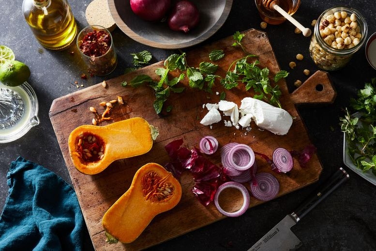On a cutting board, a bright orange squash sliced in half, tendrils of purple, and a chunk of white cheese.